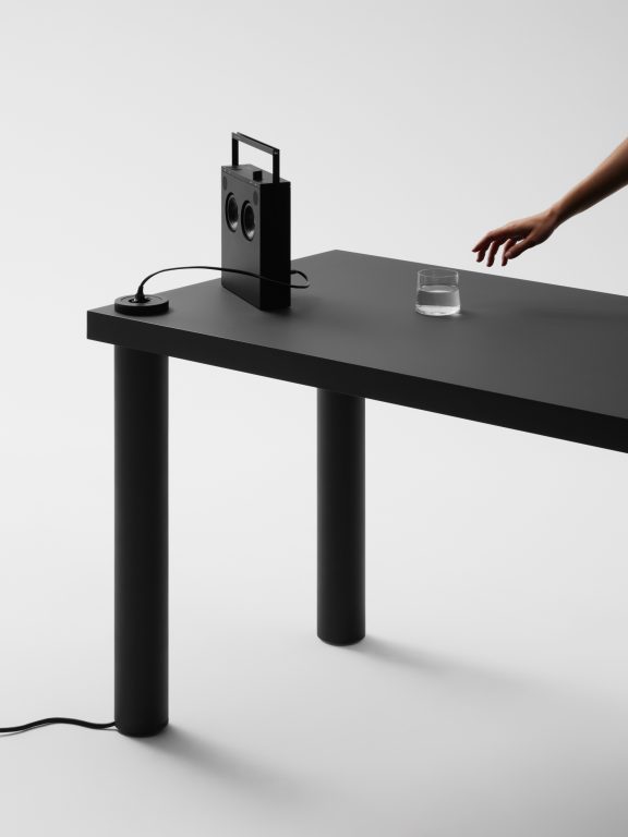 Detail of gumpo pipo table in black with power socket, dual util glass and teenage engineering radio on top.