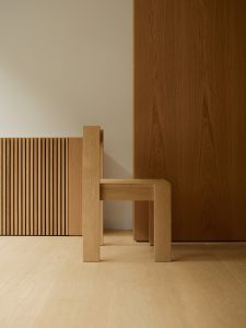 Side view of dining chair in oak in front of wall. Foeppl Collection by Relvaokellermann for Holzrausch Editions.