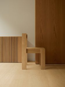 Side view of dining chair in oak in front of wall. Foeppl Collection by Relvaokellermann for Holzrausch Editions.